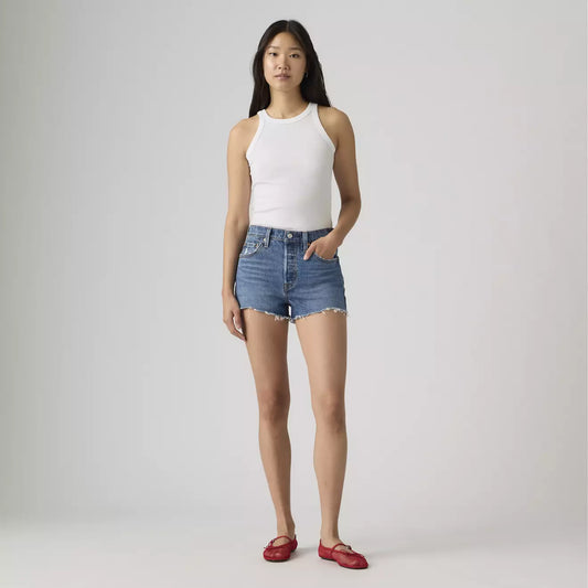 Woman wearing a white tank top and blue denim shorts on a plain background