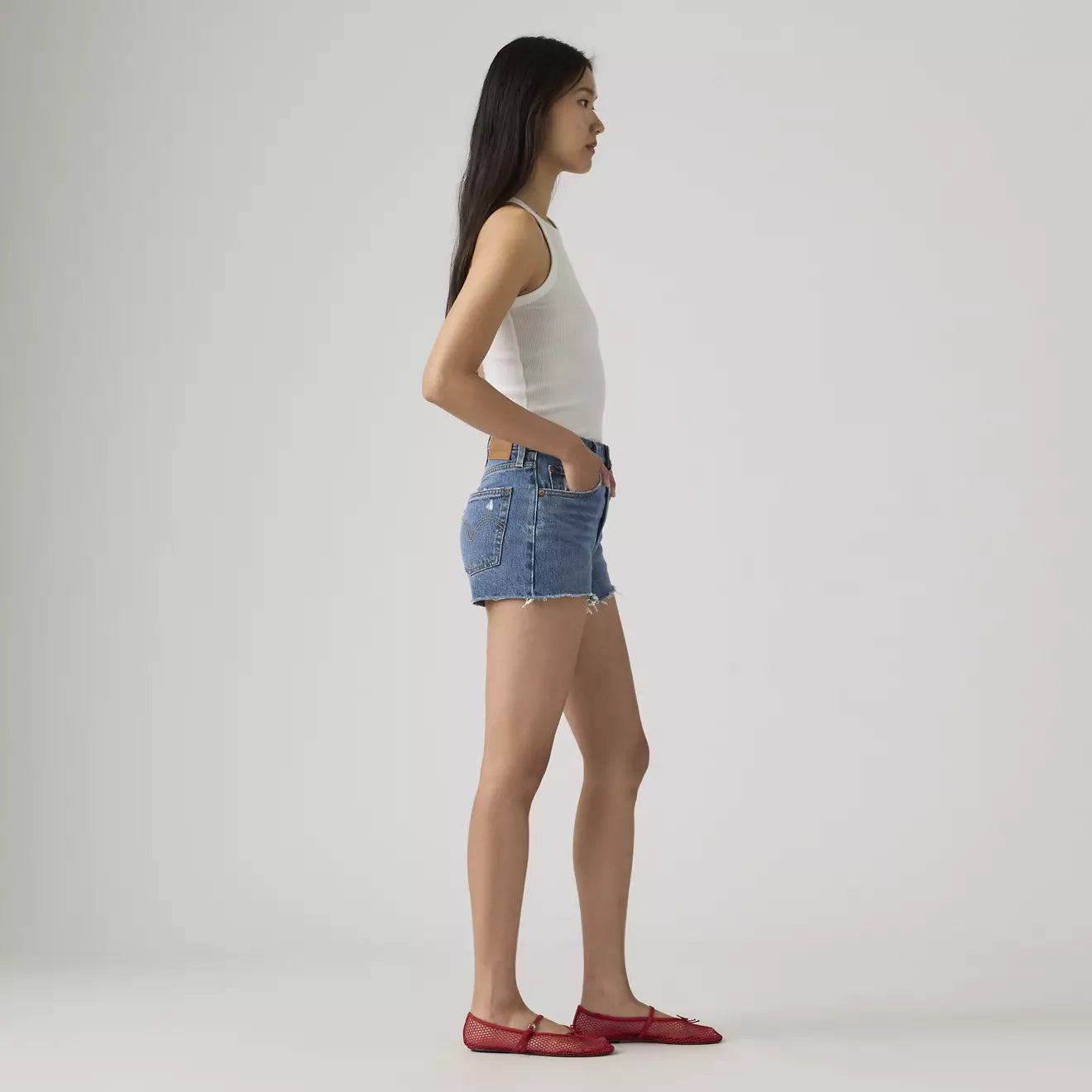 Woman wearing a white tank top and blue denim shorts on a plain background